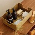 Seagrass basket holding bottles and folded cloth on a wooden surface